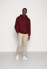 Bordó kapucnis pulóver, elülső zsebbel, bézs slim-fit nadrággal és fehér sportcipővel párosítva. Egyszerű dizájn, standard szövettextúrák.