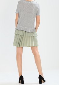 Camiseta gris a rayas con un dobladillo con volantes, combinada con una falda plisada de color verde claro. Llevada con zapatos de tacón negros.