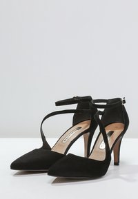Černé velurové lodičky na vysokém podpatku s špičatou špičkou, kotníkovým páskem a 10centimetrovým stiletto podpatkem. Hladký povrch s neutrálním designem stélky.