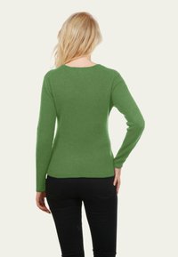 Pull vert à manches longues avec un col rond, au design ajusté et à la texture douce, porté avec un pantalon noir, vu de dos.