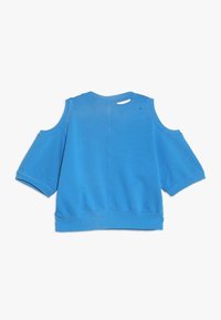 Felpa blu con maniche corte, dettagli con spalle scoperte e orlo a coste. Tessuto liscio, vestibilità informale e un piccolo strappo sul collo sul retro.