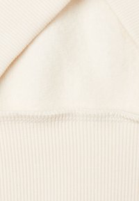 Crème trui stof, met een geribde kraag en een zachte, pluizige textuur. Zichtbare stiksels aan de zoom voegen detail toe aan het ontwerp.