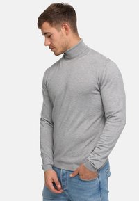 Hellegrauer Rollkragenpullover in Rippstruktur, mit langen Ärmeln und figurbetontem Schnitt, kombiniert mit blauen Jeans.