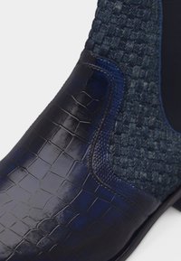 Παπούτσι από δέρμα σε σκούρο μπλε χρώμα με υφή κροκοδείλου και πάνελ από υφαντό ύφασμα, με ελαστικό πλαϊνό κομμάτι για άνετη εφαρμογή χωρίς κορδόνια.