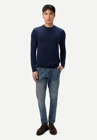 Marineblauer Rundhalspullover, figurbetonte Silhouette, aus weichem Material; kombiniert mit hellblauen Jeans und dunkelbraunen Schuhen.