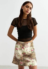 Czarna przezroczysta bluzka z krótkim rękawem i okrągłym dekoltem, w połączeniu z wzorzystą mini spódniczką w panterkę z kwiatowymi akcentami.