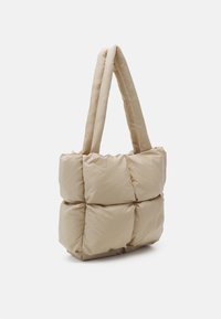 Sac fourre-tout matelassé beige avec texture matelassée, deux poignées robustes et un matériau doux et léger, présentant un design carré et sans éléments métalliques visibles.