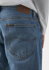 Niebieskie dżinsy jeansowe Lee w jasnym odcieniu z skórzaną naszywką marki Lee na talii, charakteryzujące się klasycznym fasonem z pięcioma kieszeniami i subtelnymi detalami przeszyć.