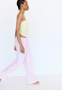Top jaune sans bretelles avec des rayures horizontales, associé à un pantalon léger et ample rose pâle. Le mannequin porte des sandales plates ; design minimaliste.