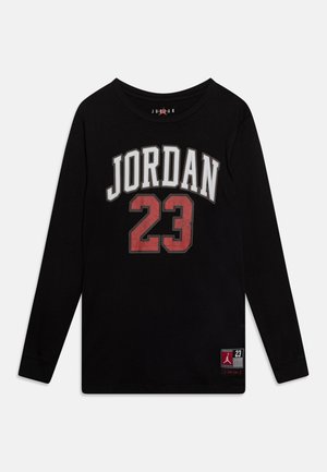 Sort langærmet skjorte med "JORDAN" i hvide bogstaver og rødt "23" nummer centreret foran, plus et lille Jordan-logo patch nær kanten.