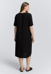 Vestido negro de longitud a la rodilla con mangas cortas, cuello redondeado y un corte suelto. El tejido parece suave y ligero, con una textura lisa.