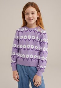 Pulover tricotat în nuanțe de liliac cu un model floral alb și accente purpurii; dispune de mâneci lungi și o margine ribbată. Este asortat cu pantaloni albaștri.