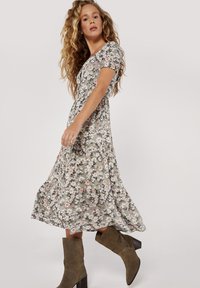 Kwiatowa sukienka midi w jasnoszarym kolorze z krótkimi bufkami, z różowymi i białymi kwiatami. Połączona z oliwkowymi botkami za kostkę.