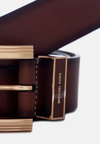 Bruine leren riem met een rechthoekige gesp in goudkleur, voorzien van een logo plaat voor Michael Kors en gestikte details langs de rand.