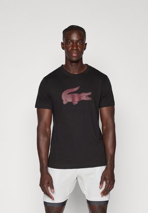 Camiseta de algodón negra con un prominente logo de cocodrilo rojo en la parte frontal. Mangas cortas y un cuello redondo clásico.