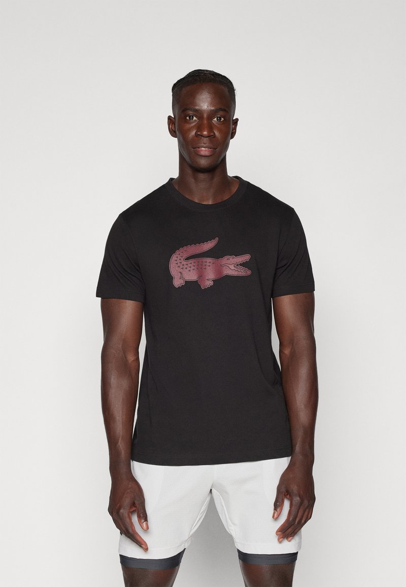 T-shirt en coton noir avec un logo crocodile rouge bien visible sur le devant. Manches courtes et col rond classique.