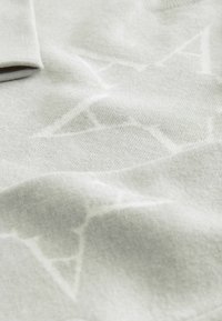 Helehall tekstil, millel on pehme, tekstureeritud pind ja õrn muster. Kangas näib olema kudumine, millel on sile ja soe tunne.