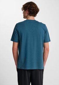 Kortärmad t-shirt med rund hals i teal bomull. Slät yta, avslappnad passform och rak fåll. Inga synliga logotyper eller mönster.