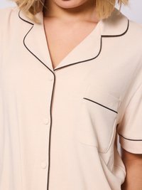 Crème-kleurig pyjamahemd met zwarte piping, korte mouwen, een borstzak en knoopsluiting. Heeft een ribbelstructuur over het hele oppervlak.
