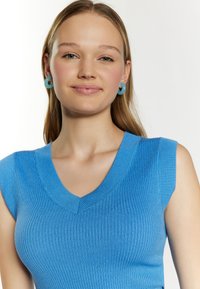 Blå ribstrikket tanktop med v-hals og korte ærmer. Har en glat tekstur og en subtil glans. Runde turkise øreringe fuldender looket.