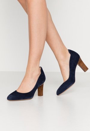 Navyblauwe suède hoge hakken met een ronde neus en een gestapeld houten hak. Het ontwerp heeft een gladde textuur en een klassieke silhouet.