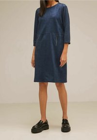 Mörkblå klänning med trekvartsärmar och rak siluett. Har två fickor med dragkedja och en texturerad tyg.