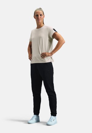 Beige athletic t-shirt with short sleeves, paired with black jogger pants, and light blue sneakers. Features a logo on the shirt's sleeve.