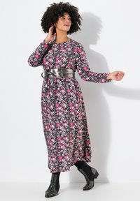 Blumenmusterkleid mit langen Ärmeln, schwarzem Grund, rosa Blumen und einem glänzenden silberfarbenen Gürtel. Getragen mit schwarzen Stiefeletten mit Nieten.