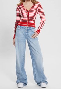 Un cardigan rayé rouge et blanc avec un col en V et des boutons en laiton, associé à un jean large bleu clair. Des baskets blanches sont portées.