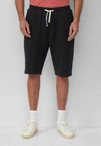 Schwarze Baumwollshorts mit einem Kordelzugbund, Seitentaschen und einem lässigen Schnitt, kombiniert mit weißen Sneakers und Socken.