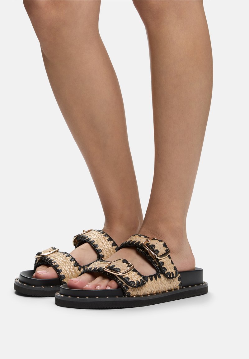 Tan and black woven slide sandals with two buckled straps, rubber sole, and decorative stitching along the edges.