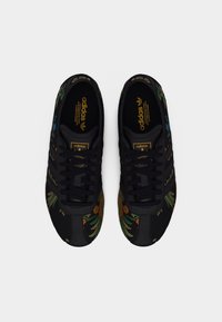 Czarne sneakersy Adidas z kolorową kwiatową haftem, czarne sznurowadła i złote logo Adidas na języku oraz wewnętrznej podeszwie, widok z góry.