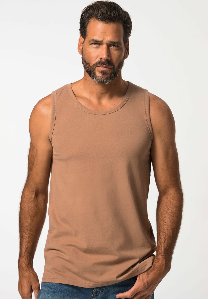 Canotta di cotone marrone con scollatura rotonda e vestibilità slim, caratterizzata da dettagli di cucitura minimi. Indossata con jeans blu. Tessuto liscio.