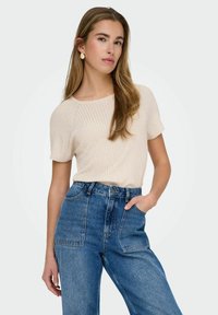 Jasnobeżowa, prążkowana bluzka z krótkim rękawem zestawiona z dżinsami o wysokim stanie i szerokich nogawkach. Gładka tekstura o minimalistycznym designie, bez wzorów.