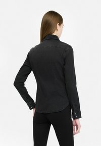 Camicia in denim nero con una forma aderente, caratterizzata da un colletto testurizzato, polsini con bottone e dettagli di cucitura sottili.