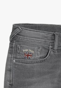 Jeans de mezclilla gris con un bolsillo frontal que presenta un logotipo bordado de "Pepe Jeans" y un diseño de la Bandera del Reino Unido. Estilo clásico de cinco bolsillos.