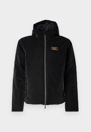 Jachetă neagră cu glugă, cu textură capitonată, având închidere cu fermoar frontal și o etichetă logo aurie pe piept. Design durabil și elegant.
