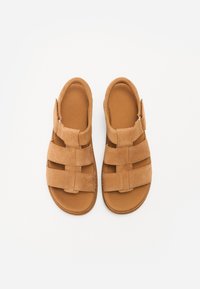 Brune suedesandaler med åpen design, som har tre brede stropper over toppen og en polstret såle for komfort.