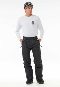 Zwarte sneeuwbroeken gemaakt van waterafstotend materiaal met een verstelbare taille, ritszakken en een losse pasvorm, gecombineerd met een wit shirt met lange mouwen.