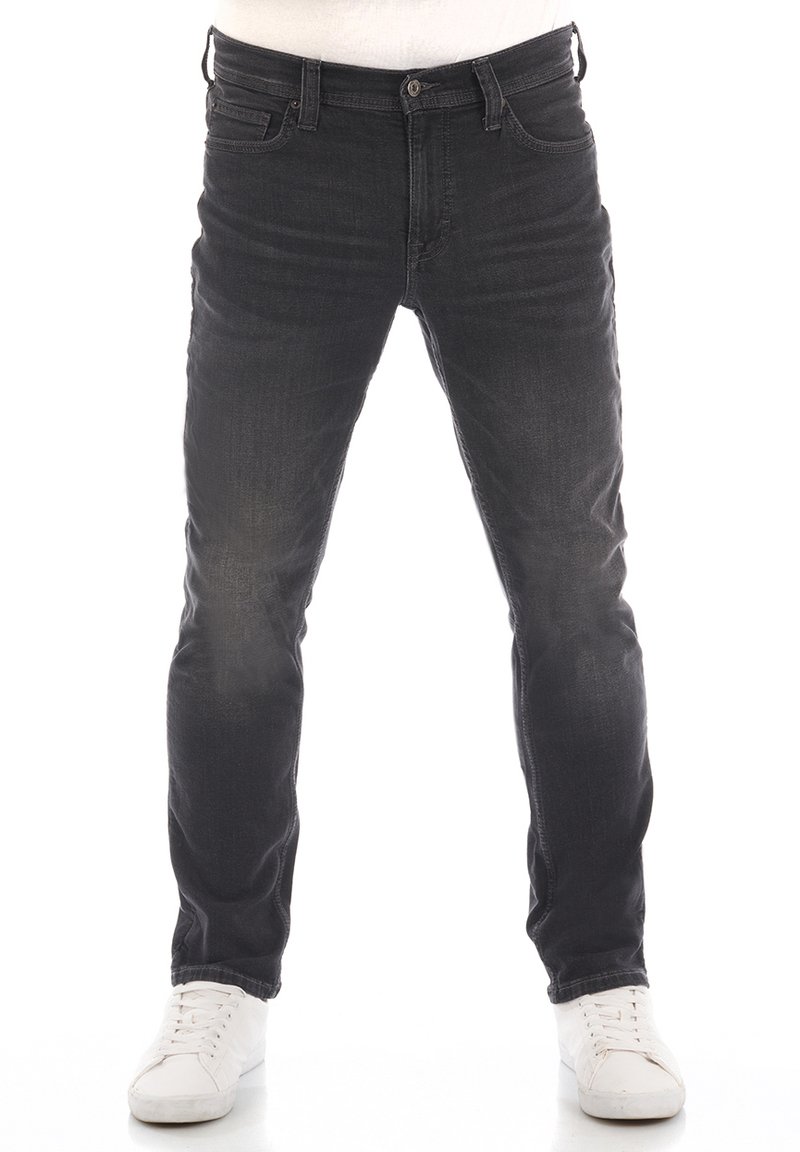 Vaqueros de mezclilla negros con corte ajustado, que presentan cinco bolsillos, un ligero desgaste y costuras en contraste. Combinados con zapatillas blancas.