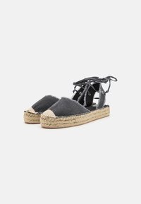 Coppia di sandali espadrillas in denim nero con suole platform in juta intrecciata e lacci da annodare alla caviglia su sfondo bianco.