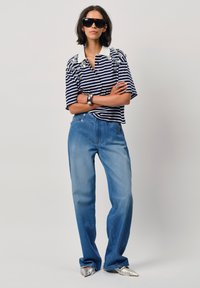 Gestreepte polo met korte mouwen en versieringen, in marineblauw en wit, gecombineerd met lichtgewassen rechte spijkerbroeken en metallic schoenen.