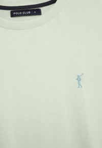 T-shirt verde chiaro girocollo con un piccolo logo ricamato blu di un giocatore di polo sul petto e un'etichetta nera "Polo Club" all'interno del colletto.