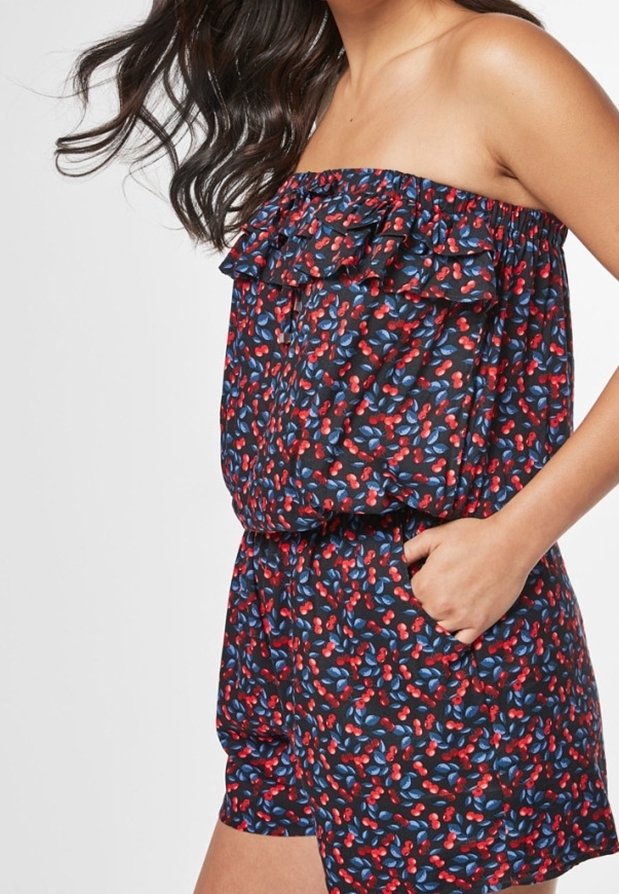 Combinaison courte sans bretelles avec un haut à volants, une taille élastique, et un tissu noir à motif floral aux tons rouges et bleus.