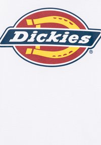 Balta marškinėliai su dideliu raudonu, geltonu ir tamsiai mėlynu ovaliu logotipu, kuriame žodis "Dickies" parašytas ryškiomis raidėmis ir dviem geltonais kreivais akcentais.