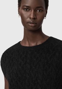 Jersey de lana negra con un patrón de punto texturizado, escote redondo y mangas cortas. La modelo lleva pendientes de aro de plata.