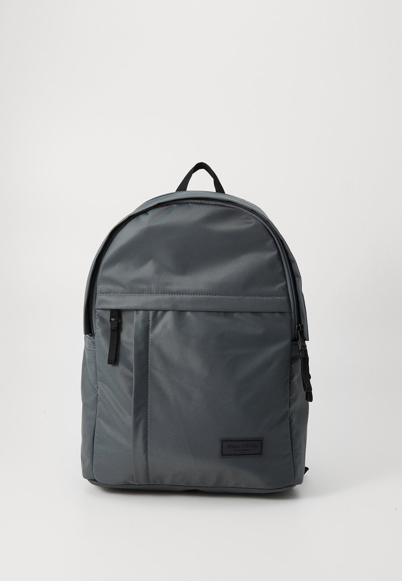 Sac à dos en tissu gris avec un dessus arrondi, compartiment principal zippé, poche avant et accents noirs. Comprend une poignée supérieure et des bretelles ajustables.