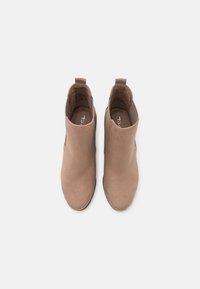 Botas de tobillo de ante marrón con paneles laterales elásticos, punta redondeada y lengüeta en la parte posterior, que presentan una textura suave y un diseño minimalista.