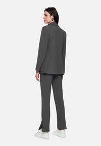 Gray tailored suit set featuring a textured fabric, front slits on pants, and a relaxed-fit jacket with a subtle collar detail. Worn with white sneakers.