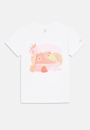 Balta marškinėliai su spalvinga grafika, kurioje pavaizduotas Converse sportbaigis, apsuptas vaisių, tokių kaip ananasas, braškės ir apelsinai.